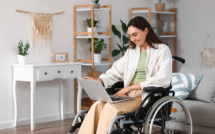 Fiona, a patient, sitting in a wheelchair at home using a laptop placed on the lap.