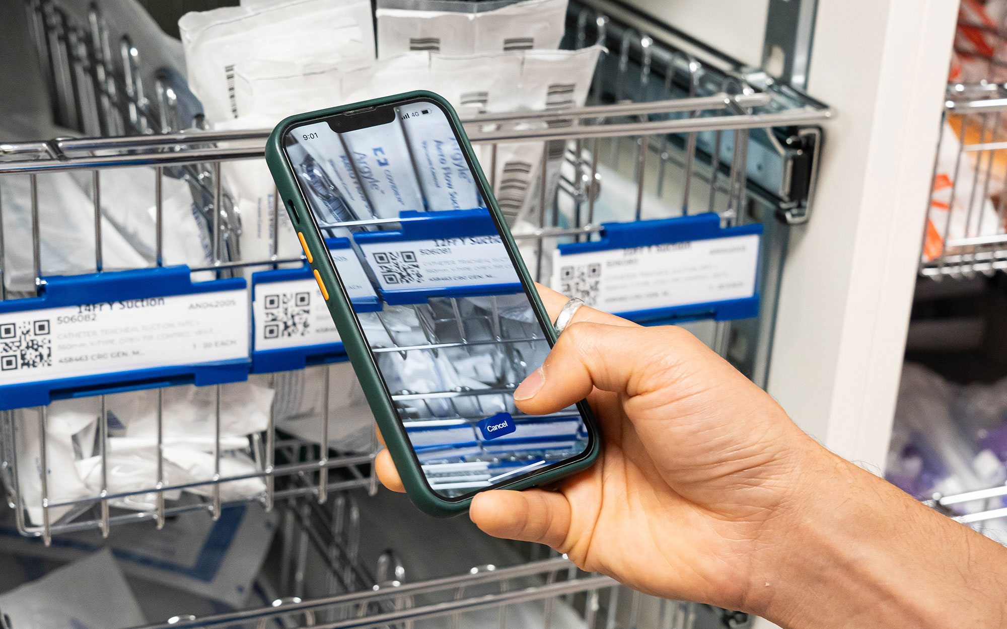 A hand holds a smartphone to scan QR‑coded medical supply labels on a storage rack.