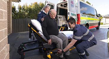 Two PTS crew members outside a patient’s house, helping an elderly person onto a gurney