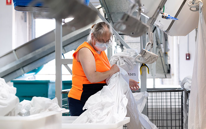 Linen Services staff member at a HealthShare NSW laundry facility, sorting through freshly cleaned hospital bed linen.