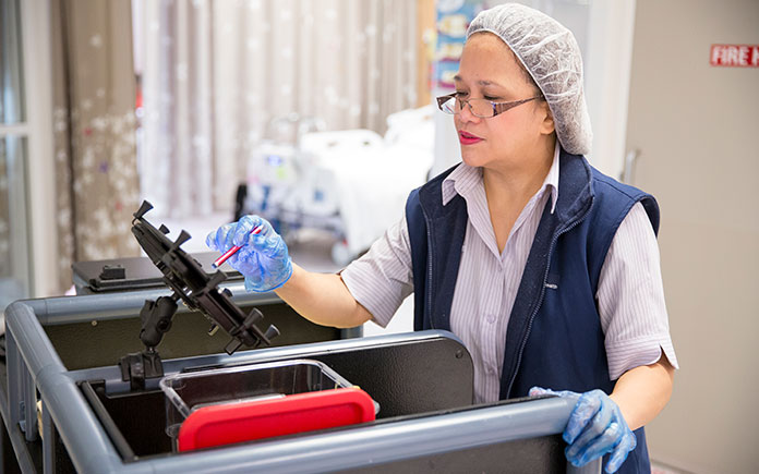 A Food Services staff member in the hospital kitchen, processing the patient meal orders on a screen.