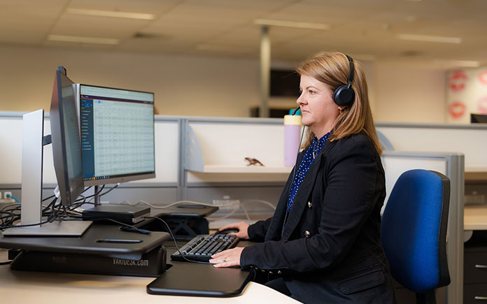 A staff member in a corporate office, sitting with a headset on at a desk processing payroll and payments.